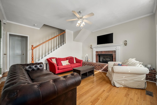 living room with ceiling fan, wood finished floors, stairs, ornamental molding, and a brick fireplace