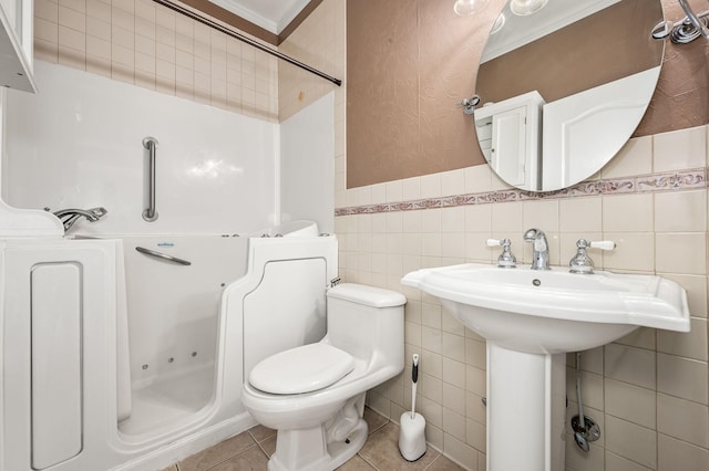 bathroom with toilet, a wainscoted wall, tile walls, tile patterned floors, and a tub with jets