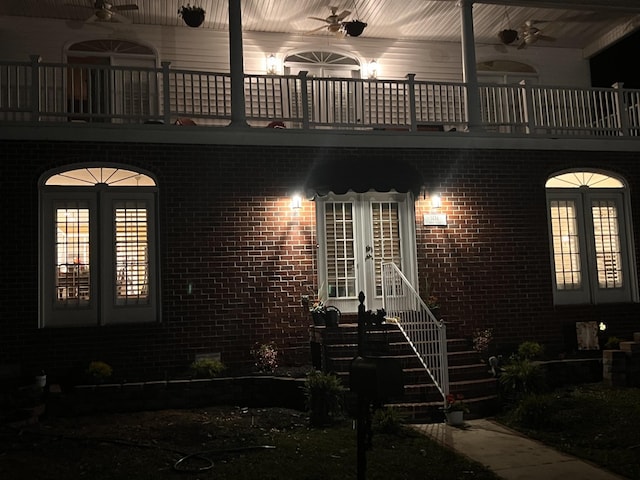 exterior entry at night with french doors, ceiling fan, and a balcony