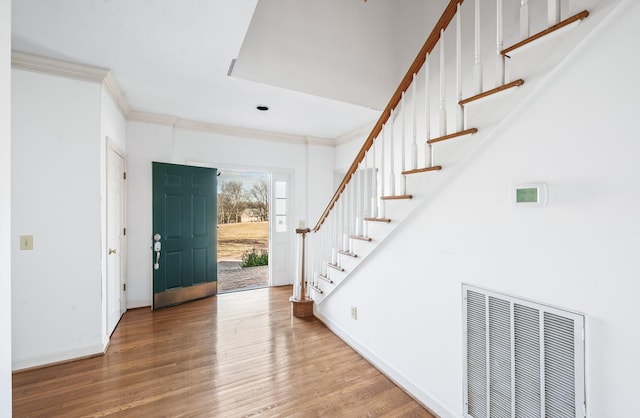 entryway with baseboards, visible vents, wood finished floors, stairs, and crown molding