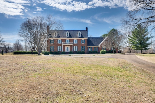 view of front of house featuring brick siding, a chimney, and a front lawn