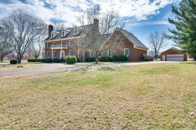 view of front facade featuring brick siding, a chimney, a front yard, a garage, and an outdoor structure