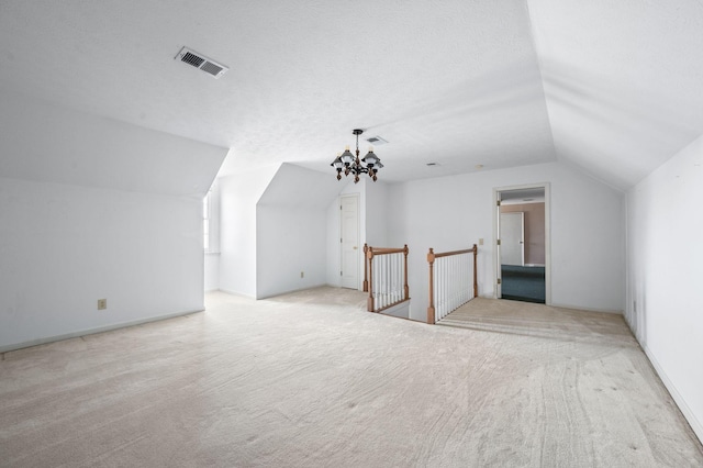 additional living space with visible vents, carpet, vaulted ceiling, a textured ceiling, and a chandelier