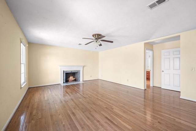 unfurnished living room featuring a fireplace with flush hearth, visible vents, ceiling fan, and wood finished floors