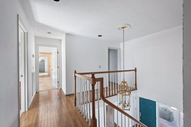 hallway with baseboards, hardwood / wood-style flooring, an upstairs landing, and a notable chandelier