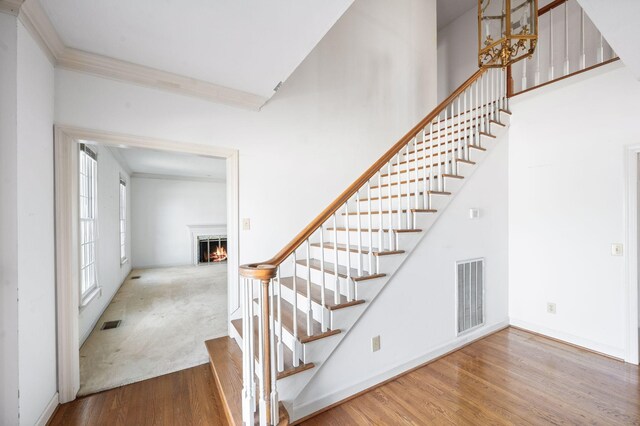 stairs featuring a lit fireplace, a high ceiling, visible vents, and wood finished floors