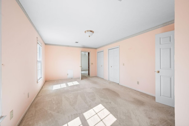 unfurnished bedroom featuring light carpet, crown molding, baseboards, and multiple closets