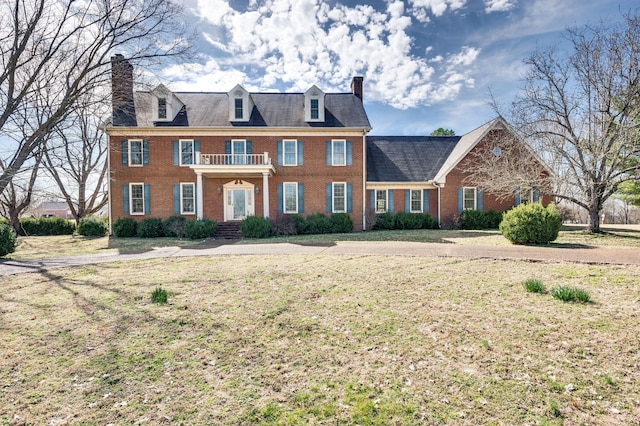 colonial house featuring brick siding, a chimney, and a front lawn