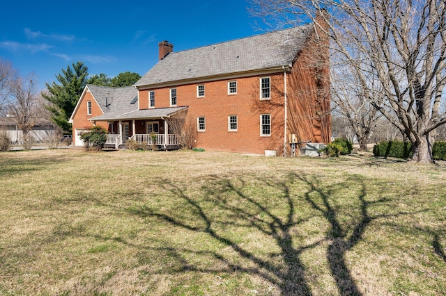 back of property featuring a garage, a chimney, covered porch, a yard, and brick siding