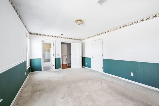 empty room featuring visible vents, carpet flooring, and wainscoting