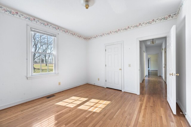 empty room featuring light wood-style flooring, visible vents, and baseboards