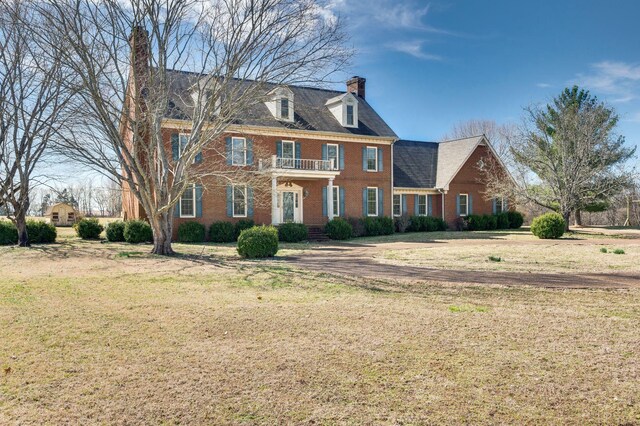 colonial house featuring a front lawn, brick siding, a chimney, and a balcony