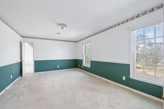 spare room with carpet, a wainscoted wall, visible vents, and baseboards