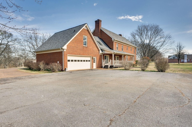 exterior space featuring a chimney, aphalt driveway, an attached garage, a porch, and brick siding