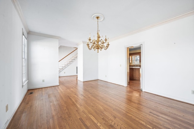 spare room with a notable chandelier, stairway, wood finished floors, and ornamental molding