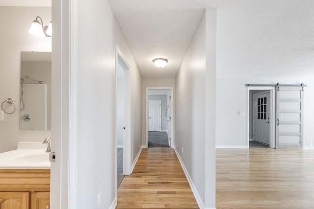 hall with a sink, light wood-style flooring, baseboards, and a barn door