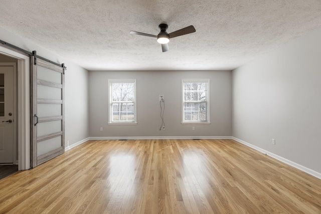 spare room with light wood finished floors, a barn door, baseboards, ceiling fan, and a textured ceiling