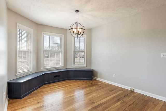 empty room with baseboards, a textured ceiling, an inviting chandelier, and light wood-style floors