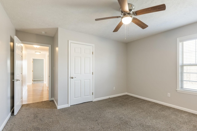 unfurnished bedroom featuring a ceiling fan, a textured ceiling, baseboards, and carpet flooring