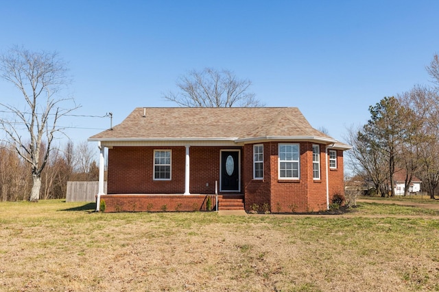 view of front of property featuring brick siding, a front lawn, a shingled roof, and fence