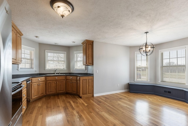 kitchen featuring stainless steel appliances, dark countertops, light wood-style flooring, brown cabinetry, and a sink