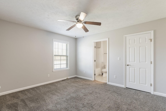 unfurnished bedroom with a textured ceiling, connected bathroom, carpet flooring, a ceiling fan, and baseboards