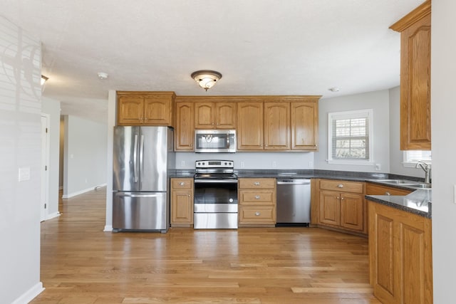 kitchen with stainless steel appliances, dark countertops, light wood-style floors, a sink, and baseboards