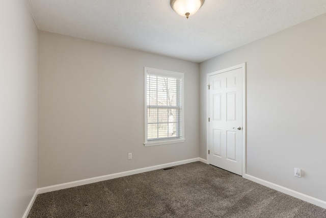 unfurnished room with baseboards, visible vents, dark carpet, and a textured ceiling