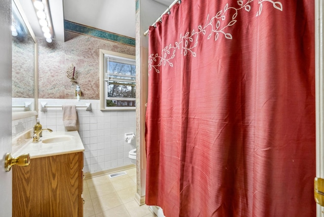 full bathroom featuring toilet, visible vents, vanity, wainscoting, and wallpapered walls