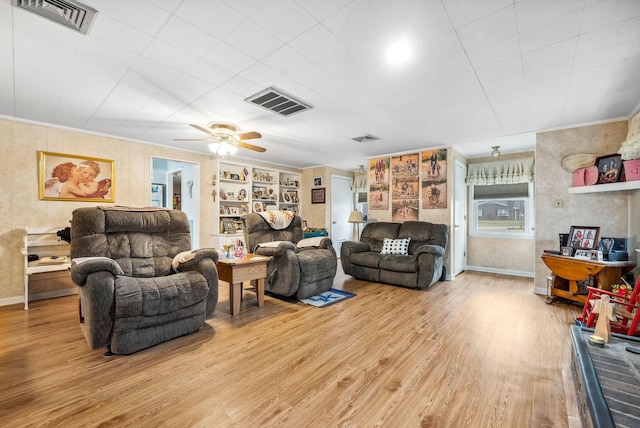 living area featuring built in shelves, light wood-style flooring, visible vents, and crown molding