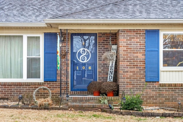 view of exterior entry with brick siding and roof with shingles