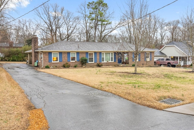 ranch-style home with driveway, brick siding, a chimney, and a front yard