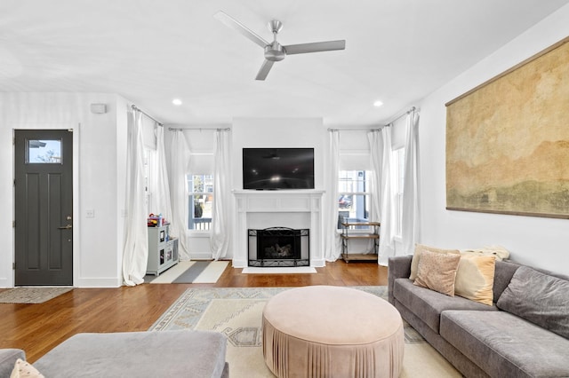 living area featuring baseboards, a fireplace with flush hearth, ceiling fan, wood finished floors, and recessed lighting