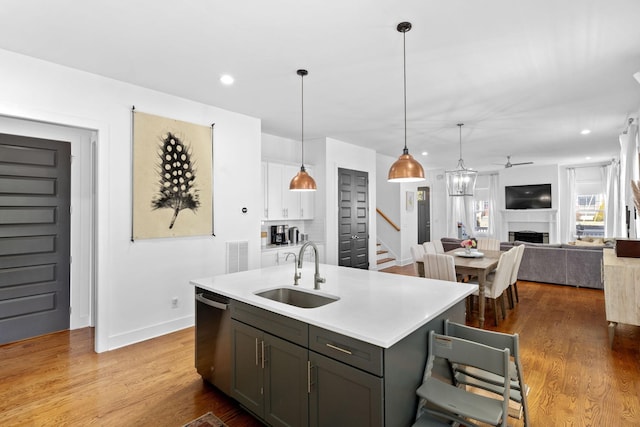 kitchen with a kitchen island with sink, a fireplace, wood finished floors, a sink, and stainless steel dishwasher