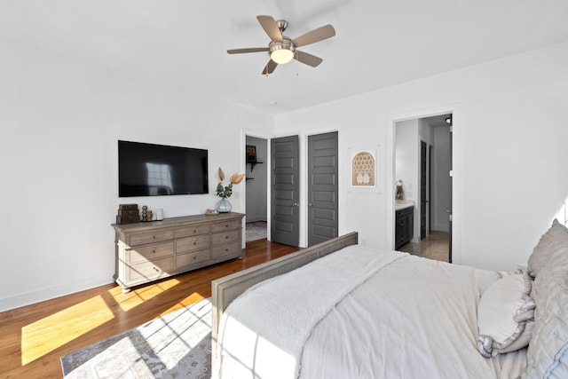 bedroom featuring ceiling fan, ensuite bath, wood finished floors, and baseboards