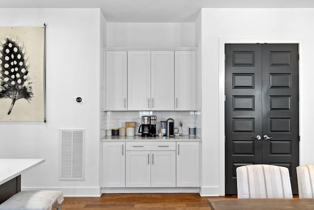 bar featuring wood finished floors, visible vents, and decorative backsplash