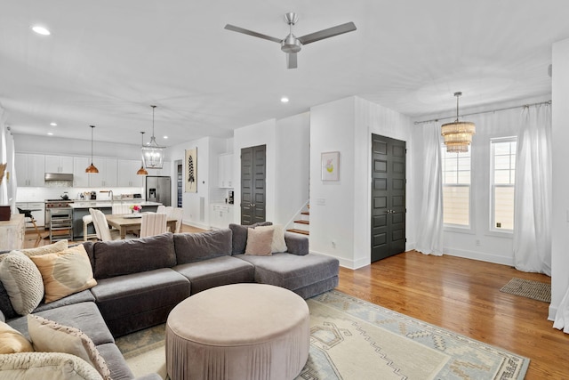 living area featuring light wood finished floors, ceiling fan with notable chandelier, stairway, and recessed lighting