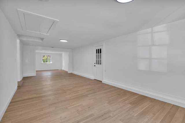 empty room featuring light wood-type flooring, attic access, and baseboards