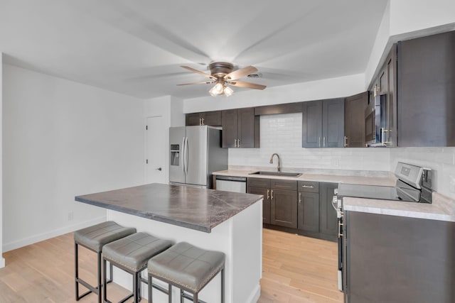 kitchen featuring a breakfast bar, light wood finished floors, tasteful backsplash, appliances with stainless steel finishes, and a sink