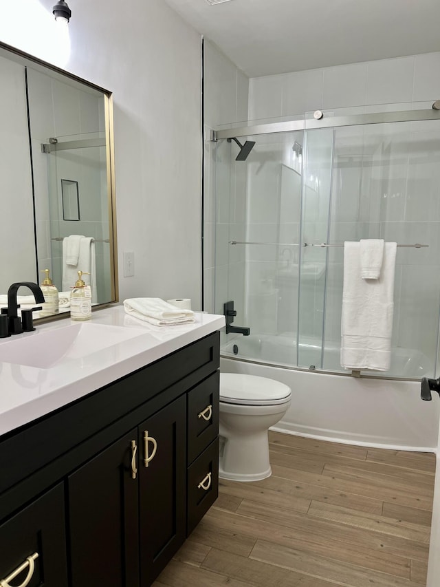 bathroom with enclosed tub / shower combo, vanity, toilet, and wood finished floors