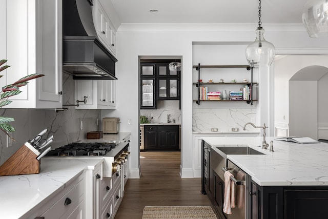 kitchen with arched walkways, dark cabinets, dark wood-type flooring, custom exhaust hood, and light stone countertops