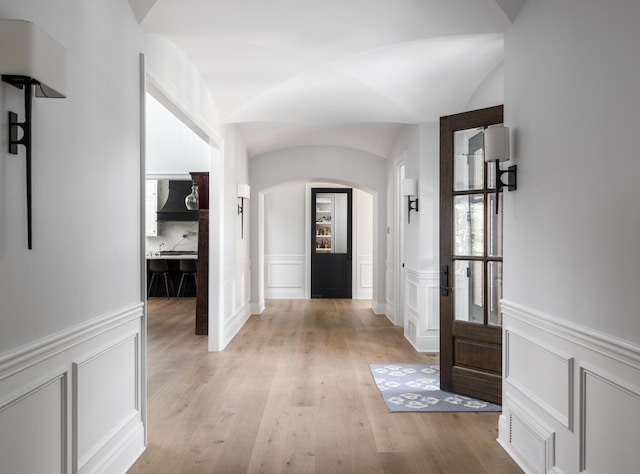 foyer with arched walkways, a decorative wall, a wainscoted wall, visible vents, and light wood-type flooring