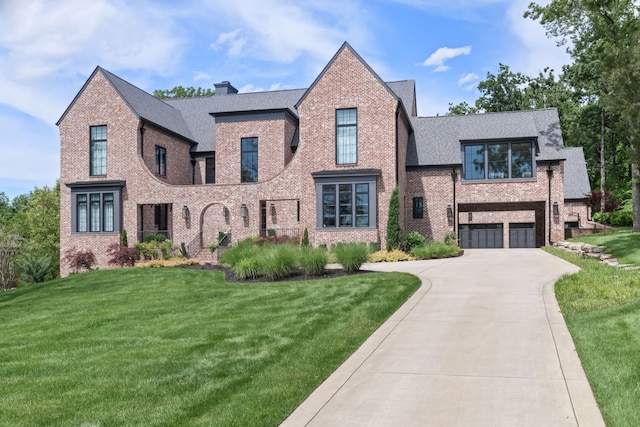 tudor-style house featuring concrete driveway, a chimney, roof with shingles, a front lawn, and brick siding