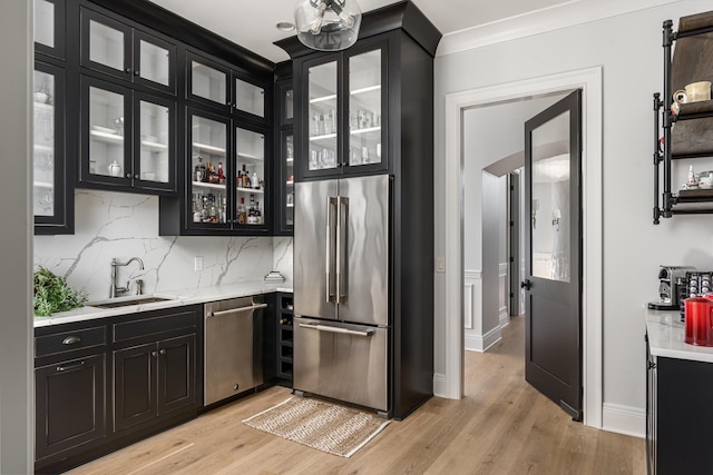 kitchen with stainless steel appliances, light countertops, a sink, light wood-type flooring, and dark cabinetry