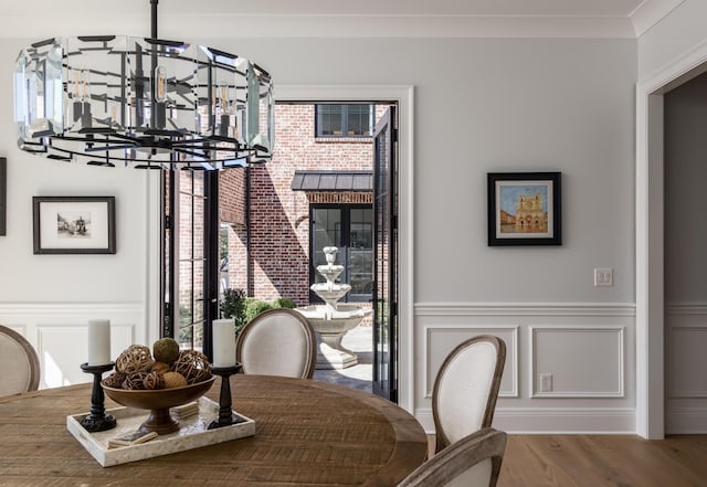 dining room with a wainscoted wall, ornamental molding, wood finished floors, an inviting chandelier, and a decorative wall