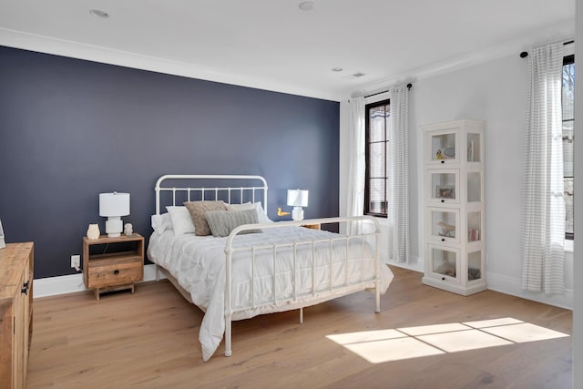 bedroom featuring light wood-type flooring, multiple windows, baseboards, and crown molding