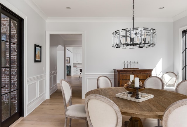 dining room with ornamental molding, a chandelier, wainscoting, and light wood finished floors