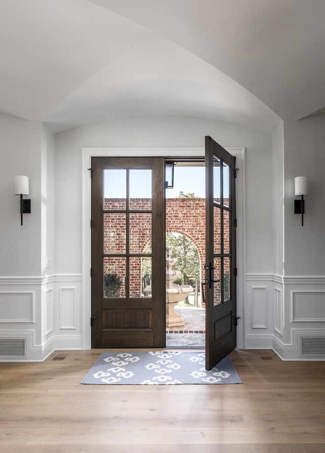 foyer featuring wainscoting, visible vents, vaulted ceiling, and wood finished floors