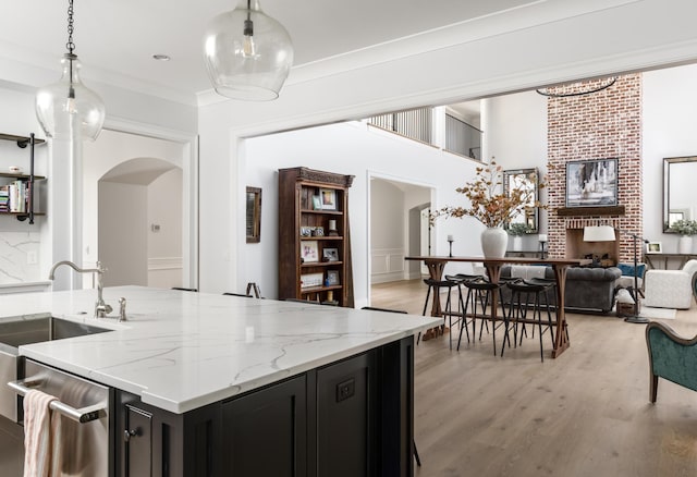 kitchen featuring arched walkways, a sink, open floor plan, dark cabinetry, and light wood-type flooring