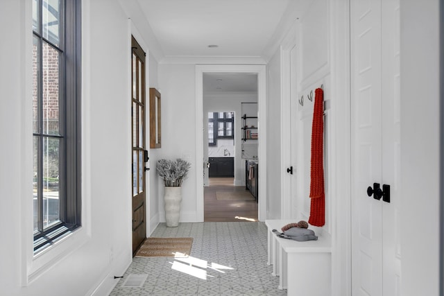 hall with ornamental molding, visible vents, a sink, and baseboards